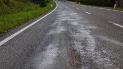 Nasse Asphaltstraße mit Wasserflecken und weißen Markierungen in einer Kurve