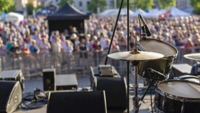 Schlagzeug mit Becken und Mikrofonständern auf einer Bühne vor einer Menschenmenge in Villach