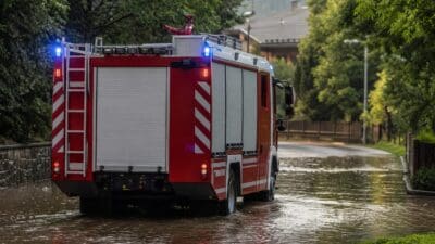 Rotes Feuerwehrauto fährt durch überflutete Straße mit Blaulicht