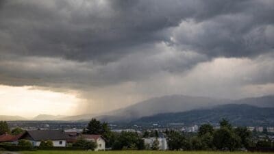 Dunkle Gewitterwolken über einer Stadt mit umliegenden Bergen und Häusern im Vordergrund