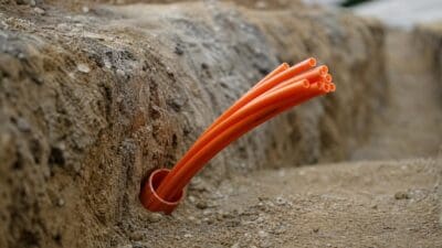 Mehrere orangefarbene Leerrohre ragen aus einem Rohr in einem Erdgraben.