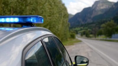 Blaulicht auf dem Dach eines silbernen Einsatzfahrzeugs an einer Straße vor Bergen