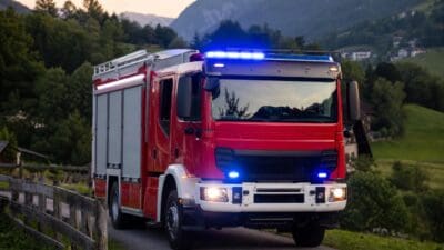 Rotes Feuerwehrfahrzeug mit blauem Blaulicht fährt auf einer Landstraße in bergiger Landschaft