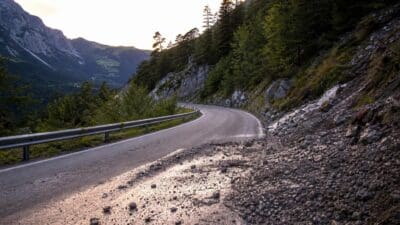 Kurvige Bergstraße mit Leitplanke und Geröll am Straßenrand in den Alpen