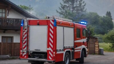 Rückansicht eines roten Feuerwehrfahrzeugs mit Blaulicht vor einem Haus in den Bergen