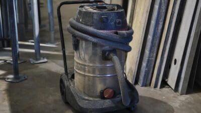 Ein dreckiger Industriestaubsauger mit Schlauch steht auf dem Boden einer Baustelle.