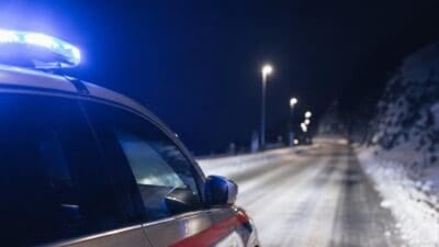 Polizeifahrzeug mit blauem Blaulicht auf einer verschneiten Straße bei Nacht