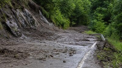 Mit Schlamm und Geröll bedeckte Fahrbahn nach Murenabgang auf der Landesstraße L19