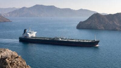 Großer schwarzer Tanker mit weißem Aufbau fährt auf dem Meer vor felsigen Bergen.