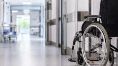 Ein schwarzer Rollstuhl steht in einem hellen Krankenhausflur mit glänzendem Boden.