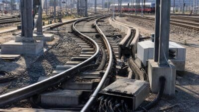 Beschädigte Kabel hängen aus Kanälen neben den Gleisen mit einem Zug im Hintergrund
