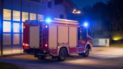 Rotes Feuerwehrfahrzeug mit aktiviertem Blaulicht vor einer Feuerwache bei Nacht
