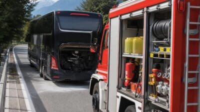 Schwarzer Reisebus mit offenem Motorraum neben rotem Feuerwehrfahrzeug auf der Autobahn