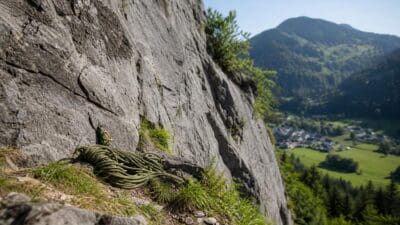 Zusammengerolltes grünes Kletterseil mit Karabinerhaken an grauer Felswand vor Bergtal