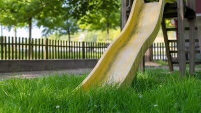 Gelbe Rutsche auf grünem Rasen in einem Spielplatz mit Holzzaun und Bäumen