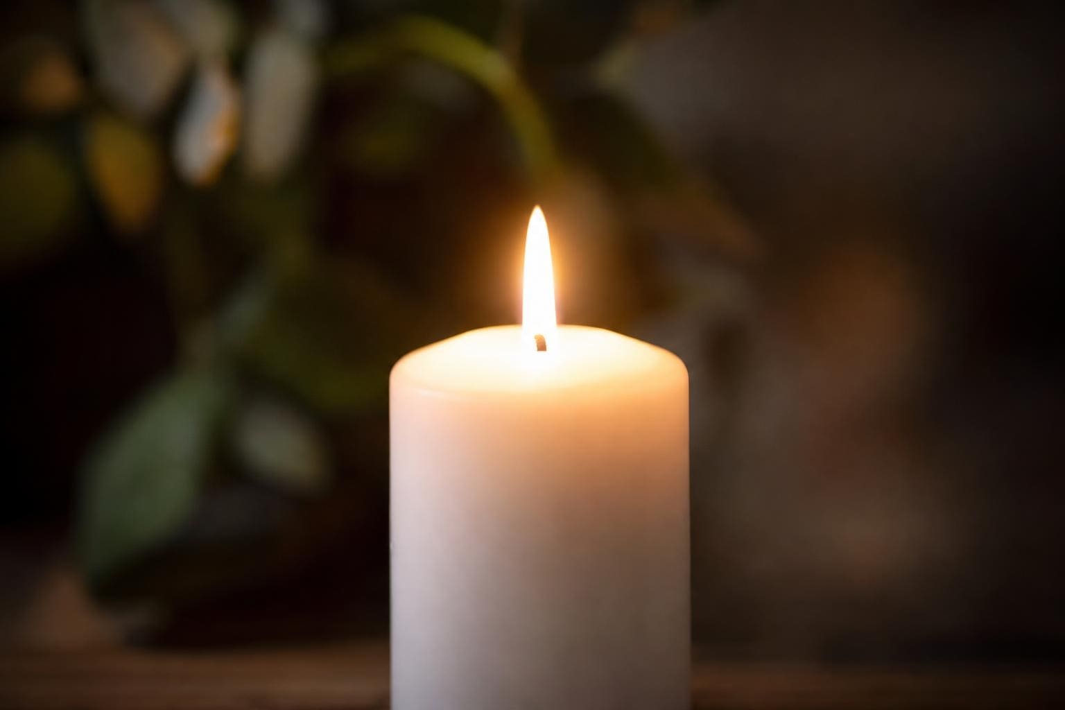 Eine brennende weiße Kerze mit heller Flamme vor einem unscharfen grünen Hintergrund.