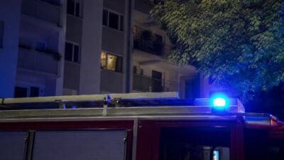 Rotes Feuerwehrauto mit blauem Blaulicht vor einem mehrstöckigen Wohnhaus bei Nacht