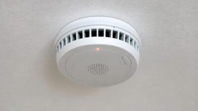 Weißer kreisrunder Heimrauchwarnmelder mit leuchtender roter LED an einer hellen Decke