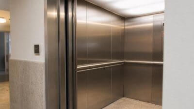 Ein leerer Aufzug mit silbernen Metallwänden, Handläufen und einem Bedienpanel auf der rechten Seite