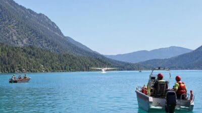 Löschflugzeug nimmt Wasser vom Weißensee auf mit Booten der Helfer im Vordergrund