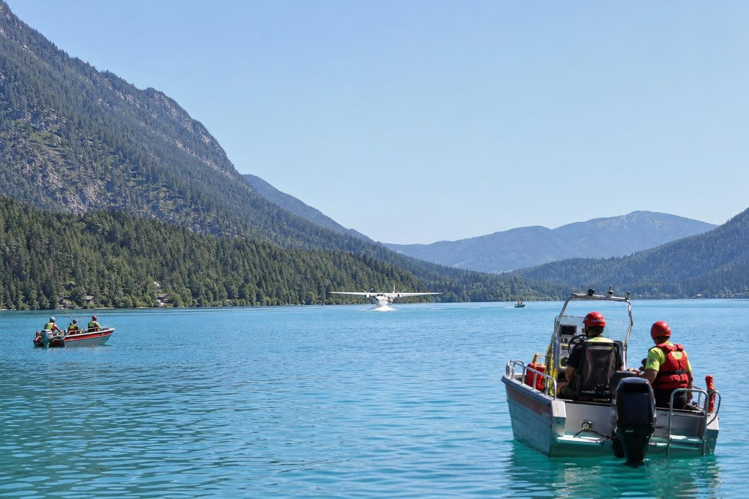 Löschflugzeug nimmt Wasser vom Weißensee auf mit Booten der Helfer im Vordergrund