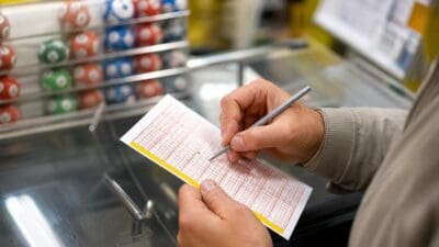 Hände halten einen Lotto-Tippschein und markieren Felder mit einem Stift.