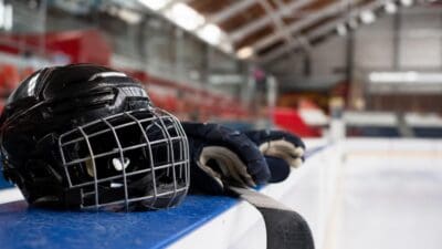 Schwarzer Eishockeyhelm mit Gitter, Handschuhe und Schläger auf der Bande einer Eishalle