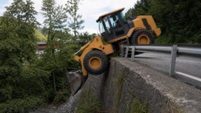Gelber Radlader hängt mit einem Rad über einer Betonmauer an der Straße