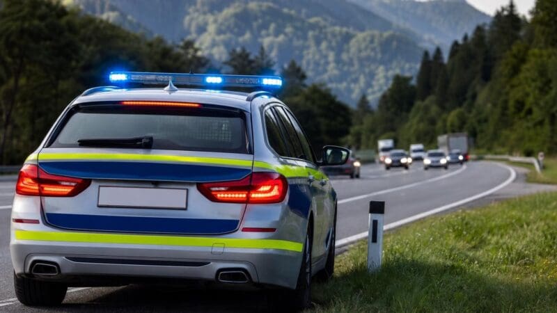 Heckansicht eines Polizeifahrzeugs mit aktiviertem Blaulicht an einer Landstraße vor Bergen