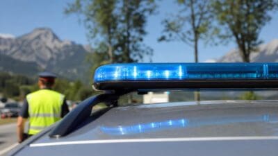 Blaues Blaulicht leuchtet auf dem Dach eines Polizeiautos mit einem Polizisten in Warnweste vor Bergen.