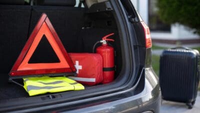Rotes Warndreieck, Verbandskasten, Feuerlöscher und Warnweste im Kofferraum eines Autos