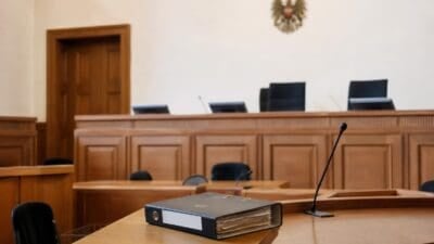Schwarzer Aktenordner liegt auf einem Tisch in einem leeren Gerichtssaal mit Holzvertäfelung