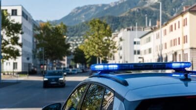 Polizeifahrzeug mit blauem Blaulicht auf einer Straße mit Gebäuden und Bergen im Hintergrund