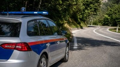 Ein silberner Polizeiwagen mit Blaulicht parkt an einer kurvigen Landstraße.