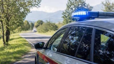 Polizeifahrzeug mit eingeschaltetem Blaulicht auf einer Landstraße in bergiger Landschaft