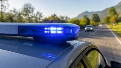Nahaufnahme des blauen Blinklichts auf dem Dach eines Polizeifahrzeugs an einer Landstraße mit Bergen im Hintergrund