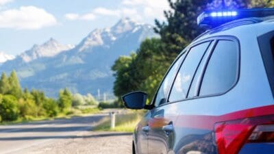 Hintere Seitenansicht eines Polizeifahrzeugs mit leuchtendem Blaulicht vor einer Berglandschaft