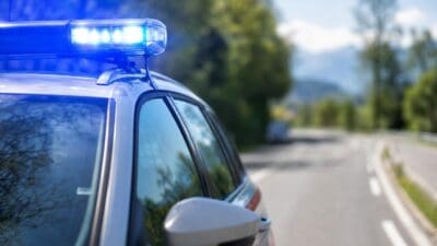 Nahaufnahme eines Polizeifahrzeugs mit leuchtendem Blaulicht auf einer Landstraße vor Bergen