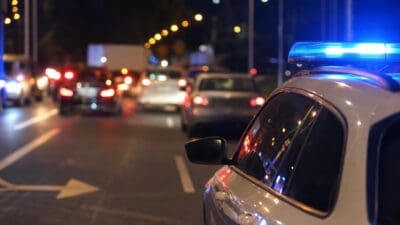 Weißes Polizeiauto mit blauem Blaulicht auf einer nächtlichen Straße im Verkehr