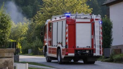 Rotes Feuerwehrfahrzeug mit Blaulicht auf einer Landstraße in ländlicher Umgebung