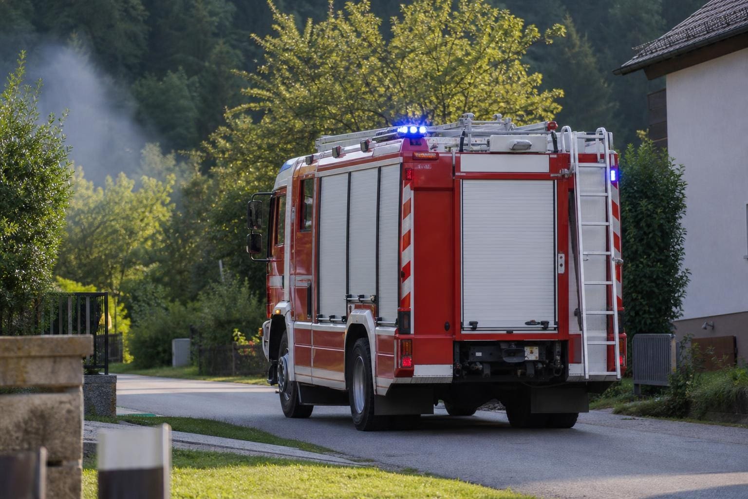 Rotes Feuerwehrfahrzeug mit Blaulicht auf einer Landstraße in ländlicher Umgebung