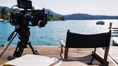 Filmkamera auf Stativ neben Regiestuhl auf Steg am Wörthersee mit Drehbuch im Vordergrund