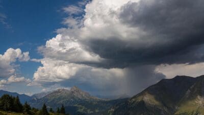 Sturmwolken entladen Regen über den bewaldeten Bergen Oberkärntens unter blauem Himmel
