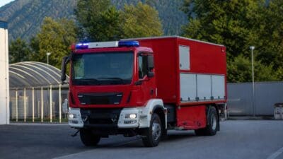 Rotes Feuerwehrfahrzeug mit Blaulicht auf dem Dach vor einer Berglandschaft