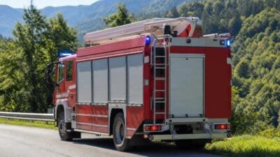 Ein rotes Feuerwehrfahrzeug mit ausgefahrener Drehleiter und Blaulicht steht auf einer Straße.