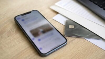 Ein schwarzes Smartphone mit beleuchtetem Display liegt auf hellem Holz neben einer grauen Kreditkarte.