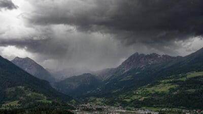 Schwere dunkle Gewitterwolken mit Regenschauern über einem grünen Bergtal und einer Ortschaft in Tirol