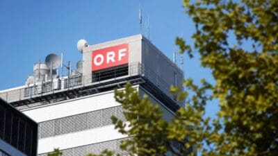 Das Dach des ORF-Gebäudes mit rotem Logo, Satellitenschüsseln und Antennen vor blauem Himmel