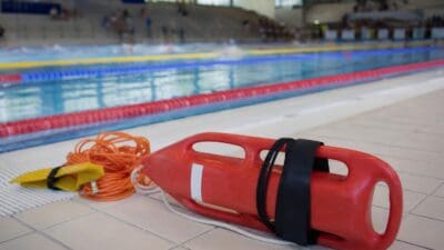 Rotes Rettungsgerät mit schwarzem Gurt neben orangem Seil am Beckenrand