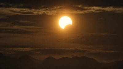 Teilweise verfinsterte Sonne als helle Sichel über einer Bergkette in Tirol